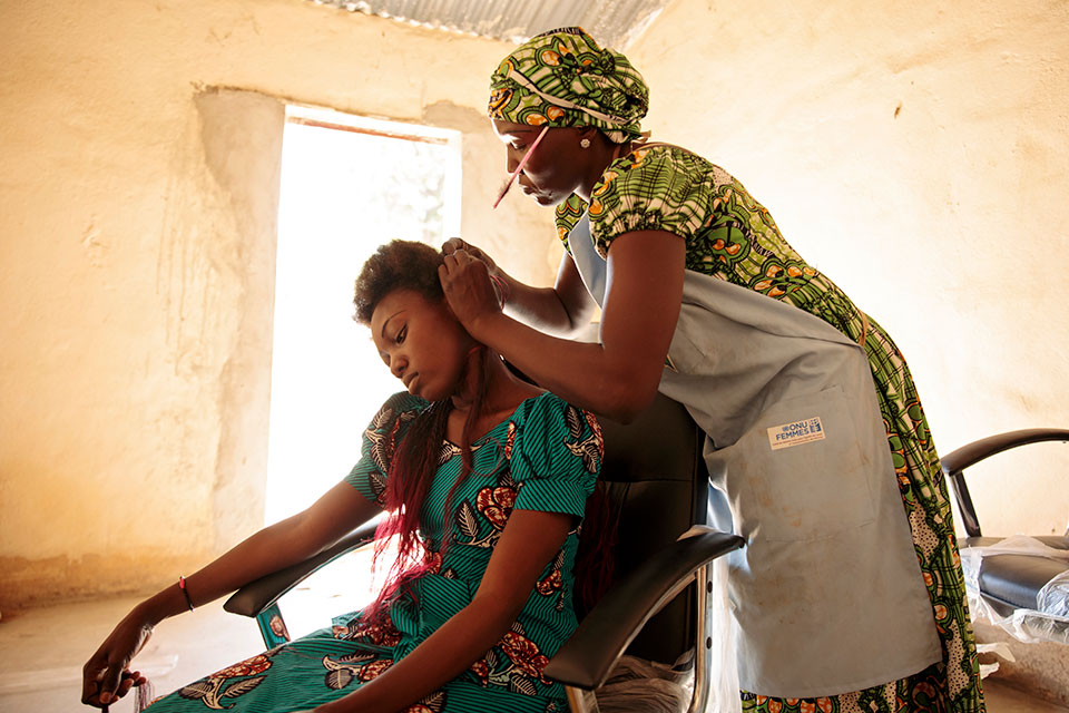 Ramata Adigre (standing) works with a client in her hair salon. Photo: UN Women/Ryan Brown