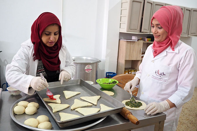 Mirvat Souri (right), a survivor of violence and a trainee at Food Incubator, listening to the instructor Samar Al-Nabahin explaining how to oil spinach staffed pastries. Photo: UN Women/Eunjin Jeong