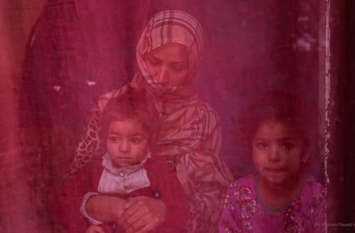 Now unemployed, a woman sits at home with her two daughters. Photo: UN Women/Sayed Habib Bidell.