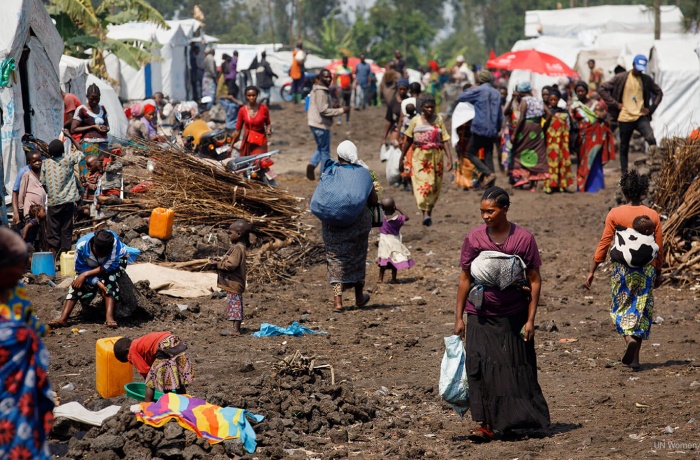 In the Democratic Republic of Congo, a woman walks through Rusayo camp for internally displaced people in August 2023. Located outside of Goma, the camp emerged as a shelter for people taking refuge from violence and, according to the World Food Programme, has grown from housing 45,000 people in January 2023 to 95,000 people by February 2024. Photo: UN Women/Ryan Brown.