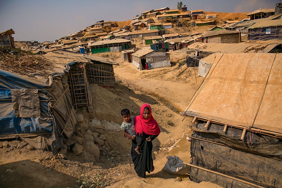 A woman walks through  Balukhali refugee camp in Cox’s Bazar, holding her child.. Photo: UN Women/Allison Joyce.