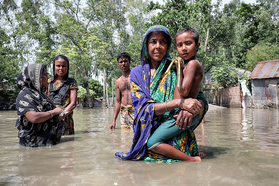 A women holds a young child in her arms while her family stands in waist-deep floodwaters.