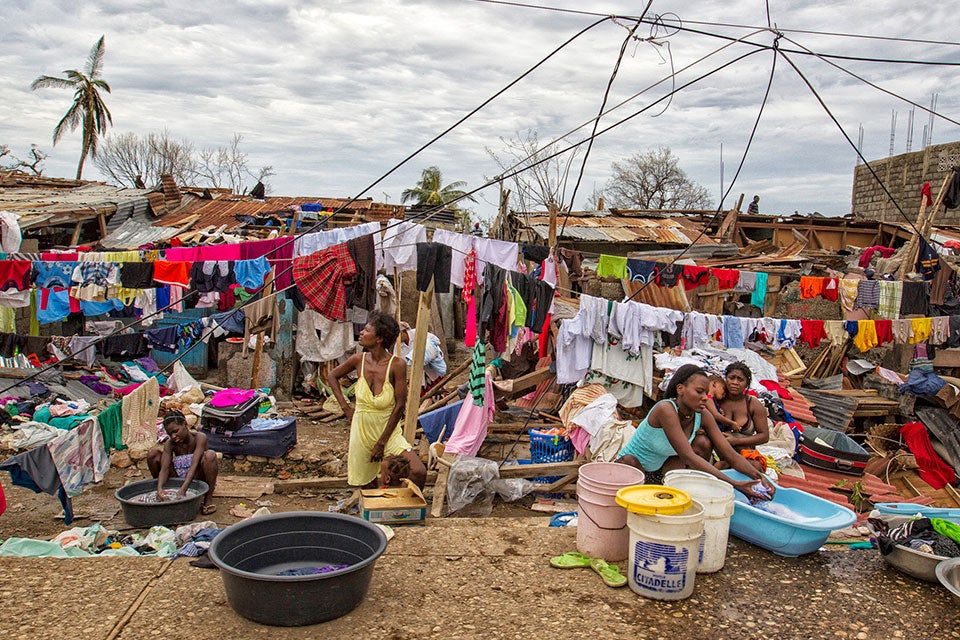 Women and girls wash clothes and care for children amid homes destroyed by Hurricane Matthew.