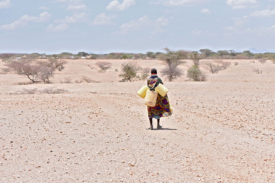 A women carries three large empty water jugs over arid land