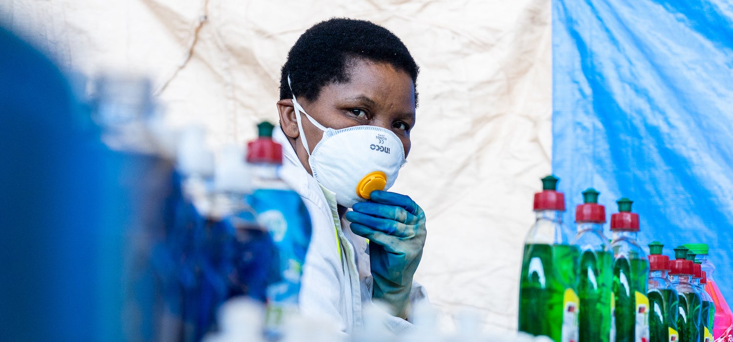 A woman in a mask and gloves with bottles of cleaning product.