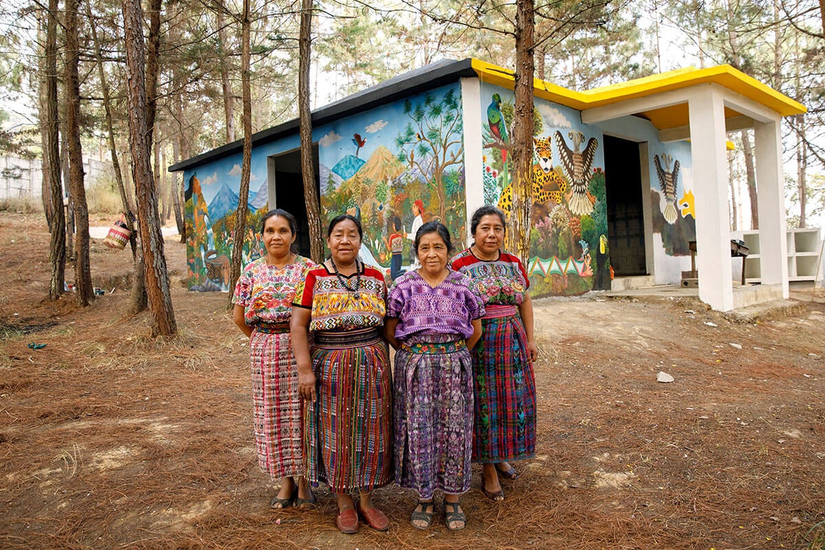 Artistas indígenas de San Juan Comalapa, Guatemala, pausan el trabajo de pintura y se toman una foto frente al Centro de la Memoria Histórica de las Mujeres, abril de 2018. En la foto, de izquierda a derecha: María Nicolasa Chex, Rosalina Tuyuc Velásquez, Paula Nicho Cumez, y María Elena Curruchiche. Foto: ONU Mujeres/Ryan Brown.