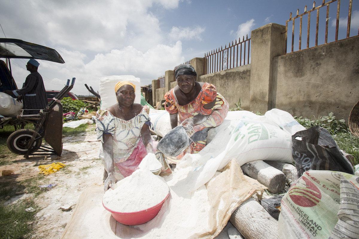 Unas mujeres venden harina de mandioca en un mercado de Abuja, Nigeria. En Nigeria, la harina de mandioca suele mezclarse con la harina de trigo elaborada con trigo importado para reducir el costo de elaboración del pan, las galletas, los bizcochos y otros productos de panadería. Fotografía: IFPRI/Milo Mitchell