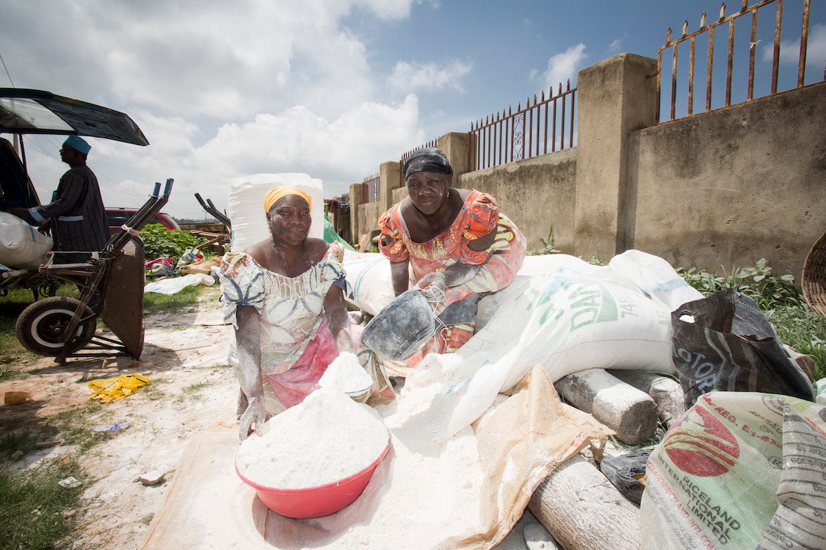 Unas mujeres venden harina de mandioca en un mercado de Abuja, Nigeria. En Nigeria, la harina de mandioca suele mezclarse con la harina de trigo elaborada con trigo importado para reducir el costo de elaboración del pan, las galletas, los bizcochos y otros productos de panadería. Fotografía: IFPRI/Milo Mitchell