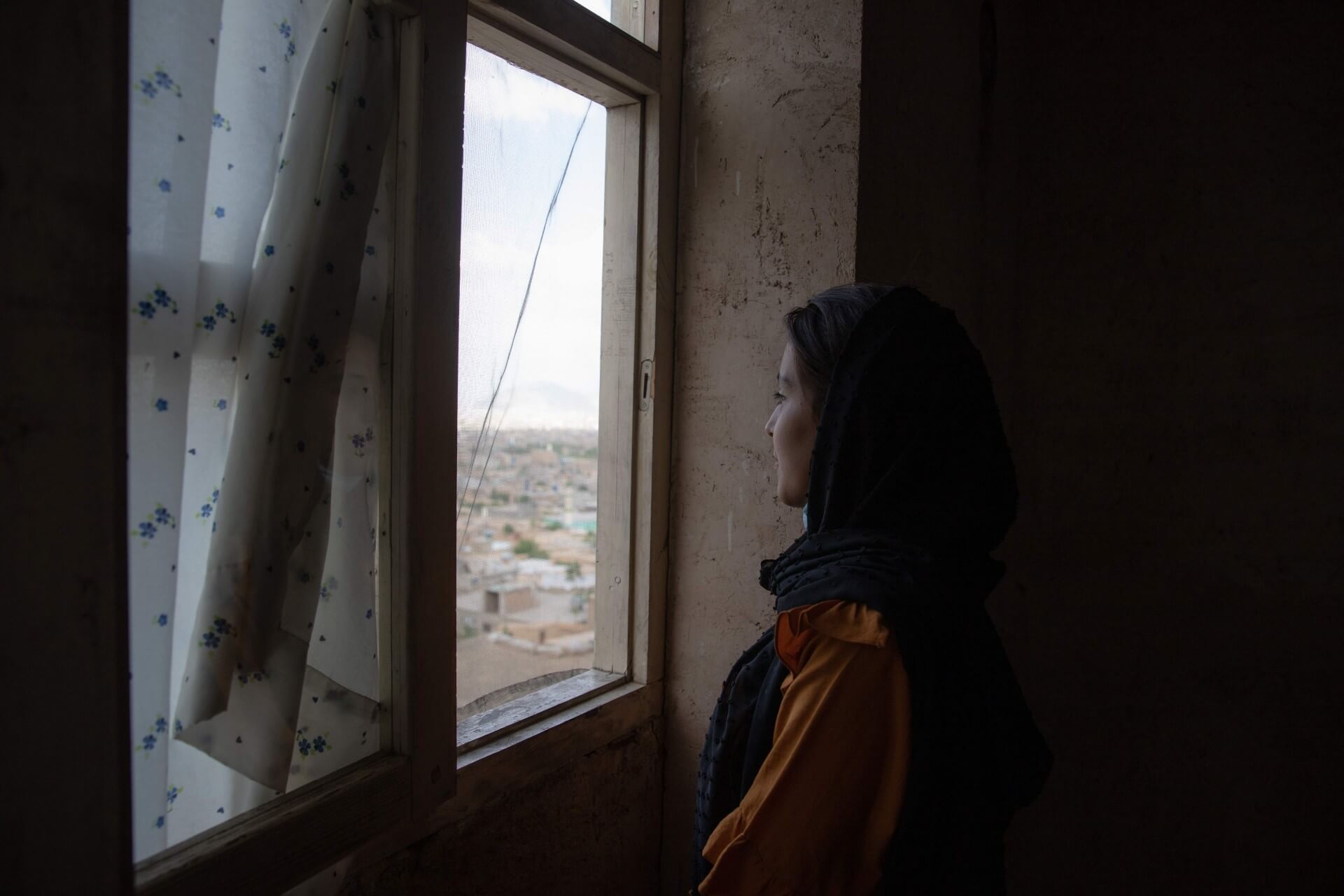 Photo of an Afghan woman looking out her window, for the “After August” in focus package. Photo: UN Women/Habib Sayed Bidell.