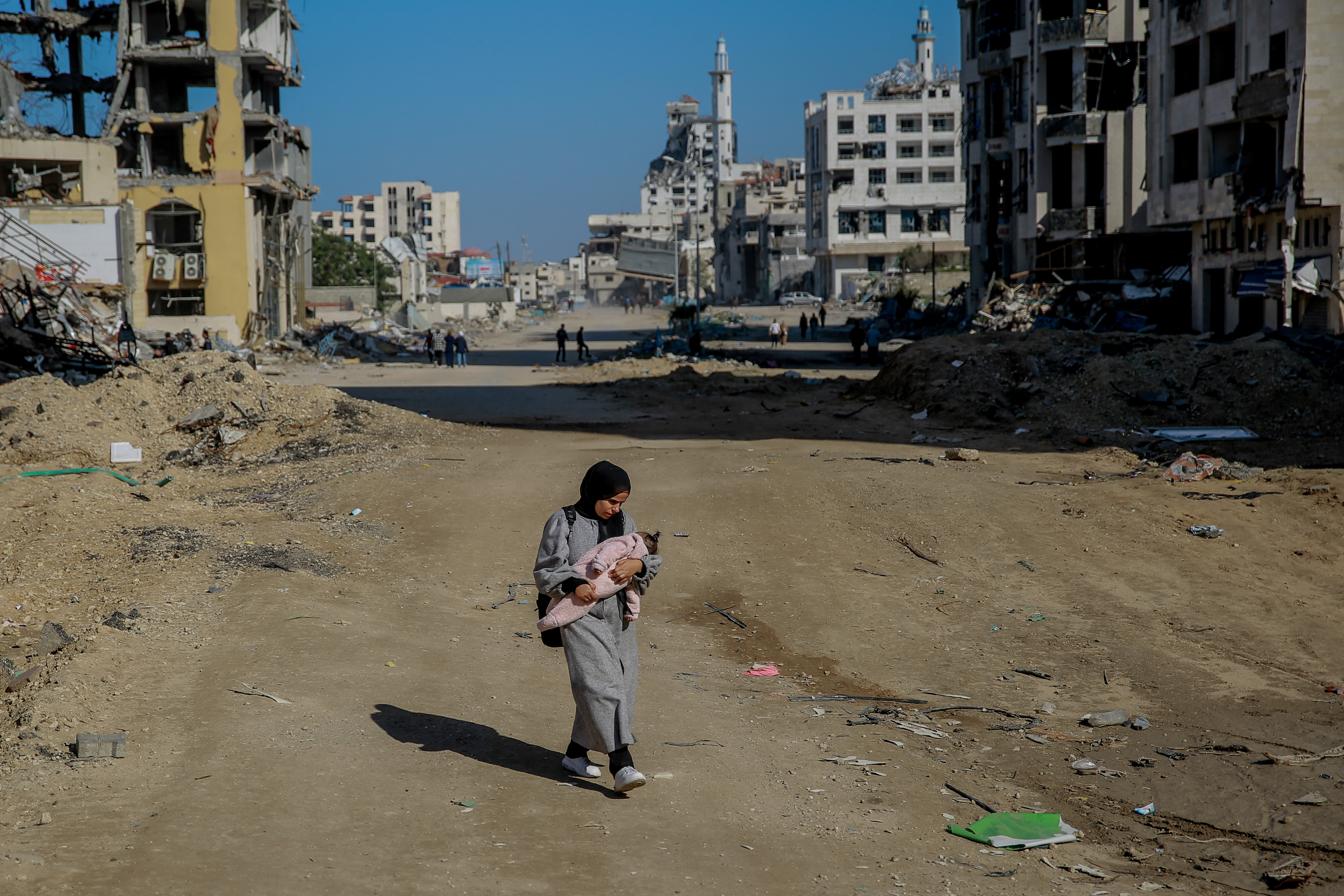 Salma, a 29-year-old, carries her infant while walking on Rashid Street, west of Gaza City, on 11 January 2024. 