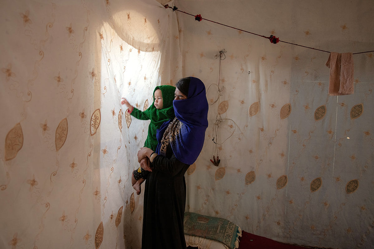 An Afghan mother holds her daughter, staring at the light from behind her obscured window. Photo: UN Women/Sayed Habib Bidell.
