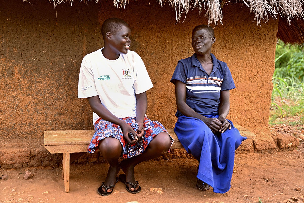 Annet Luka (at left), a South Sudanese refugee, shares a light moment with her mother outside their home in Terego, northern Uganda. Annet has already helped her family by using her new woodworking skills to make the wooden bench that they are sitting on.