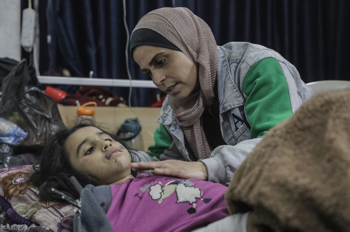 An injured child lays on a hospital cot while a women comforts her