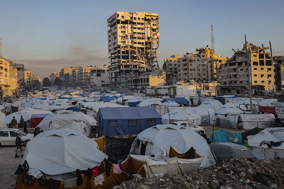 Hundreds of white tents sit below shelled out buildings in Gaza City.