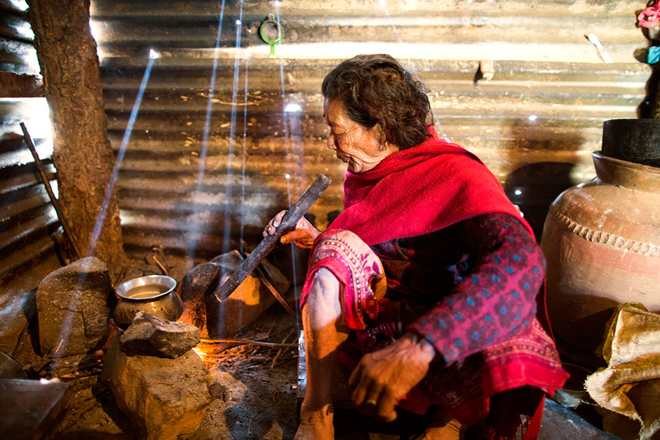 This is home. Home for seventy-two year-old Bishnu Maya Dangal who is blowing to light up the fire for cooking. Photo: UN Women/N. Shrestha