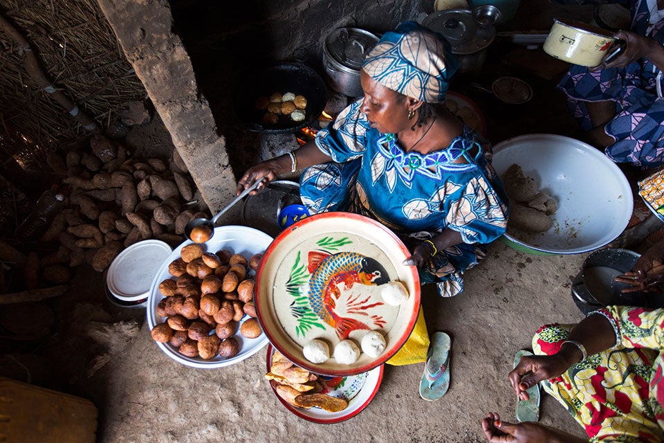 Inside a thatched hut built around a stove made of mud bricks, refugee women work together to prepare food for their afternoon customers. Photo: UN Women/Ryan Brown