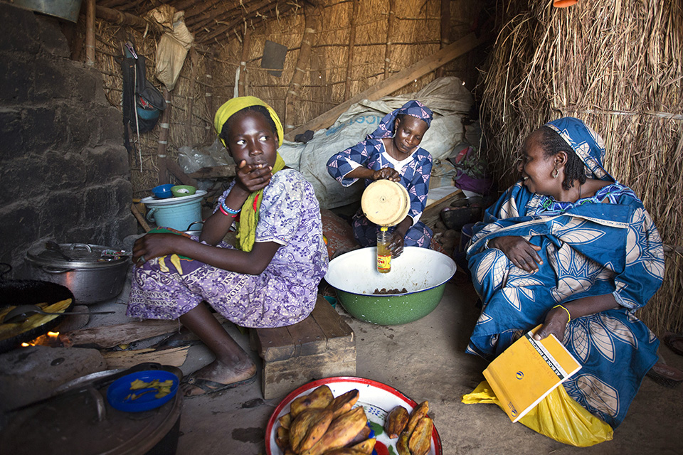 Nene (centre) and one of her daughters, Salamatou Abubakar (left), 12, have been providing food to many refugees at a makeshift restaurant in a small market at the camp. Photo: UN Women/Ryan Brown