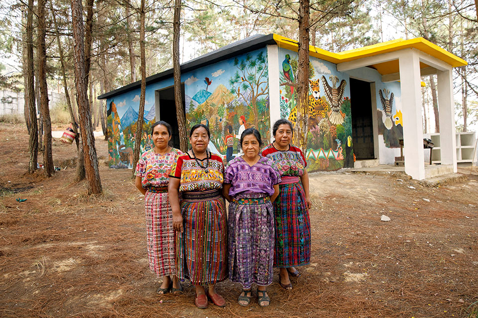 The artists from Comalapa pause painting work and stand with Rosalina for a photo in front of the memorial. Pictured from left to right: María Nicolasa Chex, Rosalina Tuyuc Velásquez, Paula Nicho Cumez, and María Elena Curruchiche. Photo: UN Women/Ryan Brown