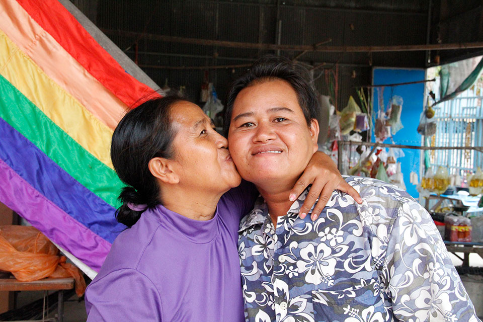 By the flag of LGBT pride, Sao Mimol kisses her partner during an LGBT PRIDE event organized by Cam ASEAN, a Cambodian human rights group supported by UN Women. Photo: UN Women/Mariken Harbitz