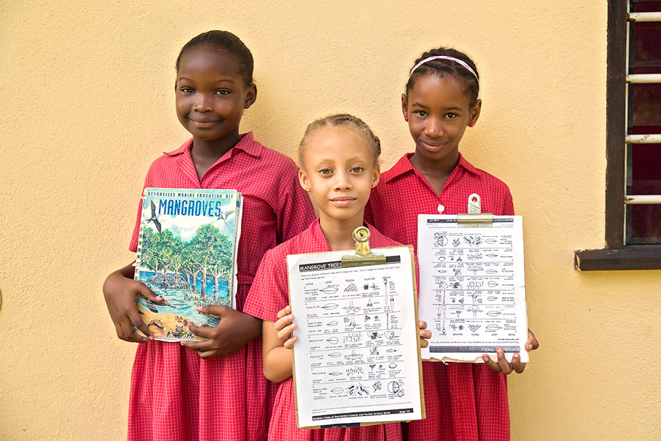 Young girls in Seychelles show off their schoolwork on Mangroves. Photo: UN Women/Ryan Brown