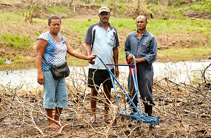 Lusiana Bulu (Secretary of the Ba Market Vendors Association) with Rakesh Prakash and his brother Sanesh Kumar on their farm just outside of Ba. Flooding destroyed much of the crops, leaving them with bare twigs and rotten eggplants. Photo: UN Women/Murray Lloyd