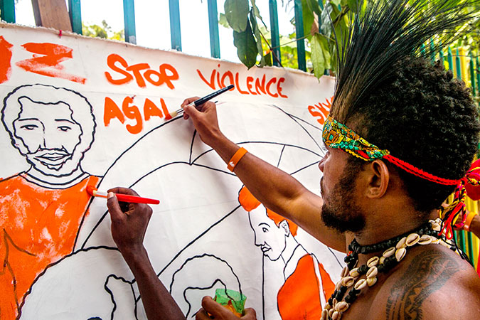 An event attendee colors a banner at an "Orange the World" event at Gerehu Market in Papua New Guinea. Photo: UN Women/Johaness Terra