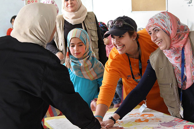 Hadeel Al-Zoubi, in orange, leading creative activities with Syrian refugee children to commemorate World Refugee Day in 2015 at the UN Women Oasis in the Za’tari refugee camp. Photo: UN Women/Christopher Herwig