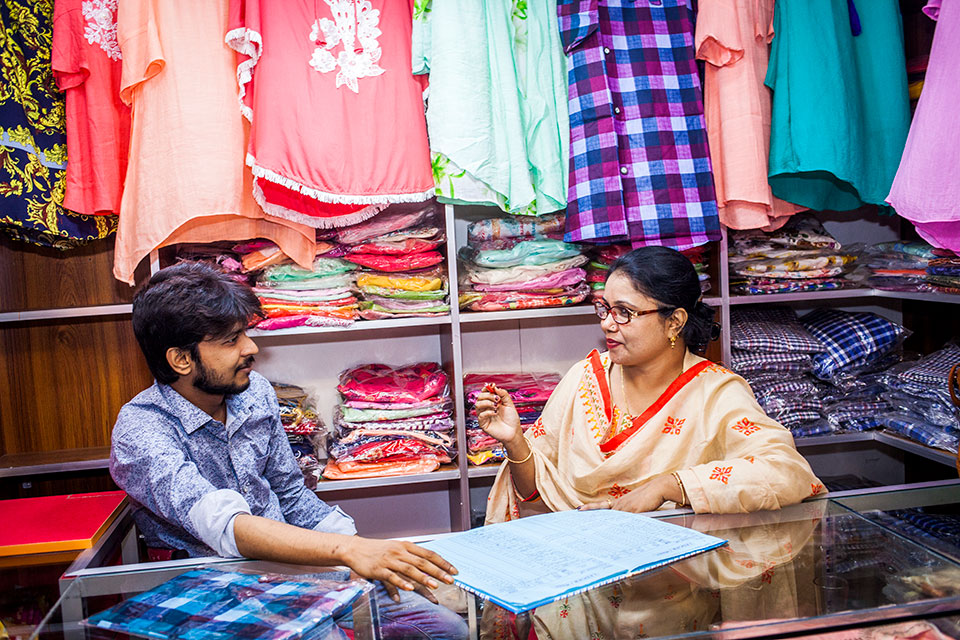 Parveen Akter, at right, owner of Glamour Fashion House, overseeing business with her elder son, Ridoy, at Jessore Bazar area. Photo: UN Women/Fahad Kaizer