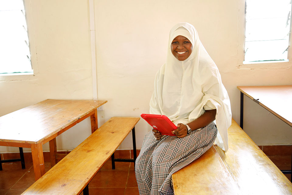 Mumina Khalif sits with a tablet computer in the classroom used for computer class and the ICT club. Photo: UN Women/Ryan Brown