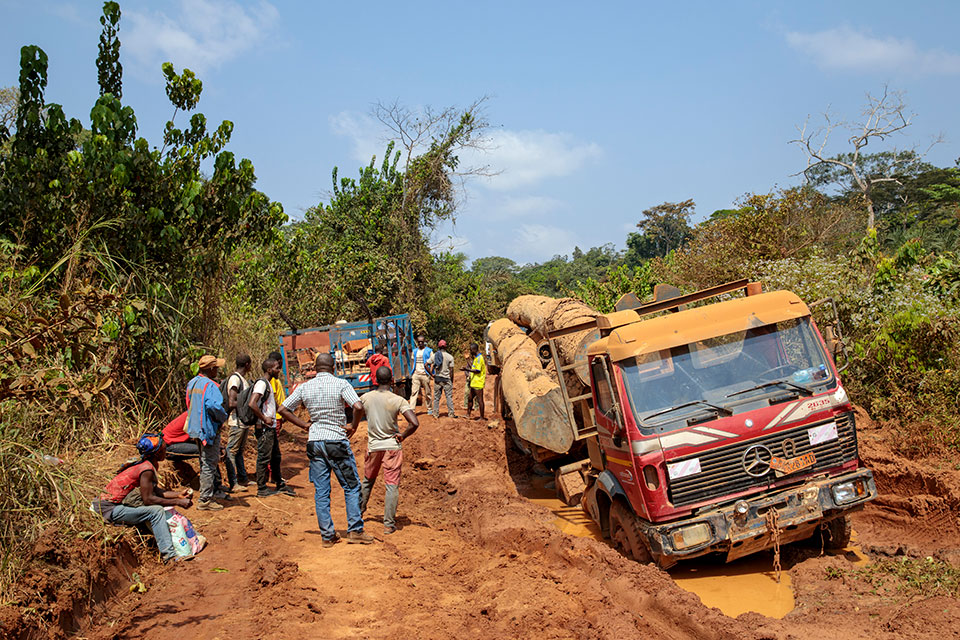 Large trucks temporarily block the road in both directions as the muddy dirt surface is unable to sustain the traffic and heavy loads put upon the only regional roadway. Photo: UN Women/Ryan Brown