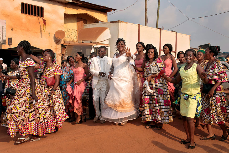 A wedding party walks down the main street of Ntui on a Saturday evening temporarily stopping traffic and sharing their celebration. Photo: UN Women/Ryan Brown