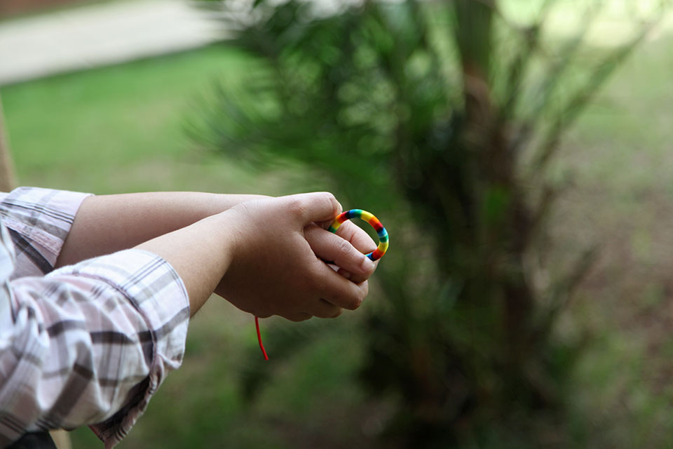 hands hold a beaded rainbow bracelet. 