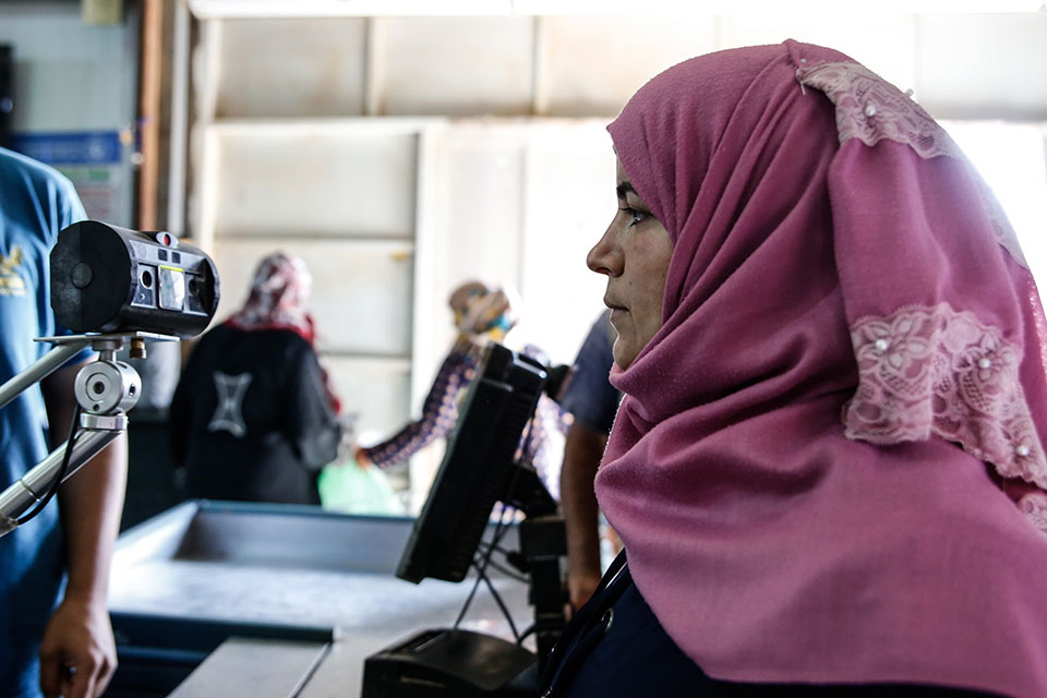 Avant l’introduction des mesures de confinement, une bénéficiaire du programme d’ONU Femmes se soumet à une procédure permettant de scanner son iris, ce qui lui permet d’acheter des produits alimentaires au supermarché du centre commercial Sameh, dans le camp de réfugiés d’Azraq, en Jordanie. Photo : ONU Femmes/Lauren Rooney.