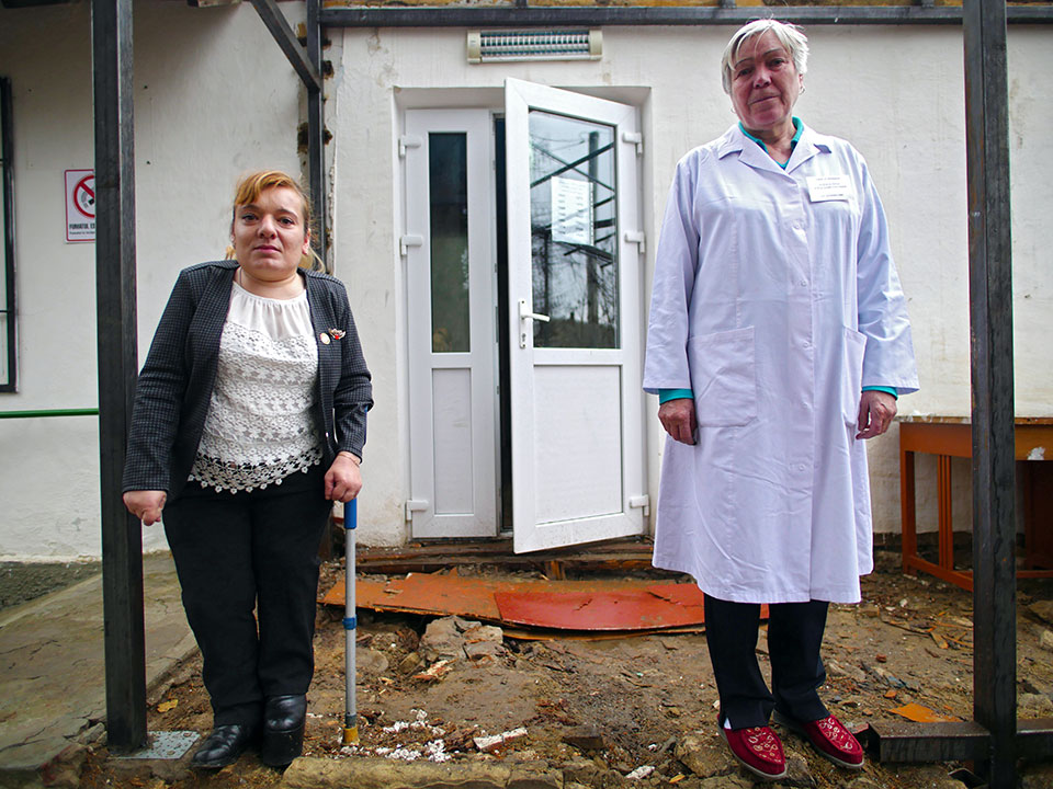 Elena Crasmari (left), pictured in 2019, stands with a staff nurse in front of the inaccessible entrance to the village medical centre. After becoming councilor Crasmari’s work contributed to the renovation of the medical centre. Photo: UN Women/Tara Milutis