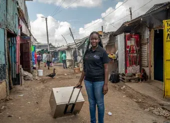 Norah Magero poses for a photo with the Vaccibox, an innovative solar-powered fridge made by her organization Drop Access using locally available materials. Photo: RAEng/GGImages/Alissa Everett.