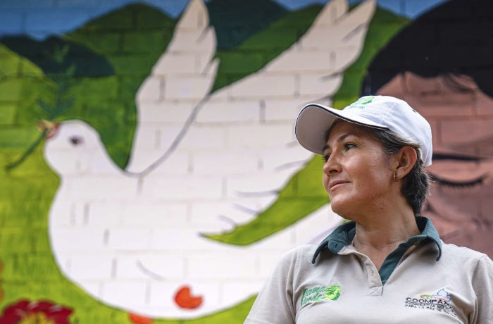 A woman stands in front of a painting of a dove. 