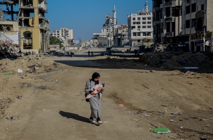 Salma, a 29-year-old, carries her infant while walking on Rashid Street, west of Gaza City, on 11 January 2024. 